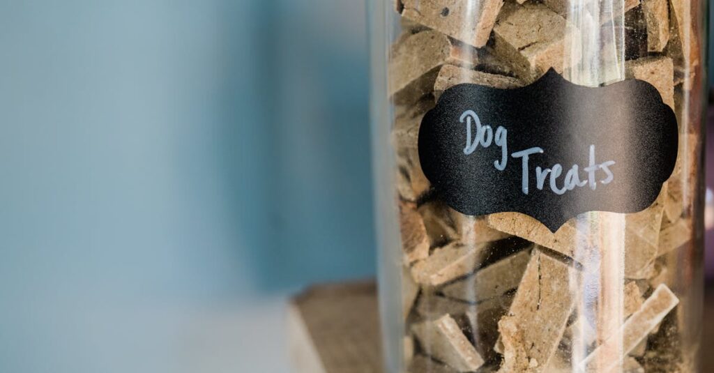 A close-up image of dry dog treats stored in a labeled glass jar on a wooden surface.